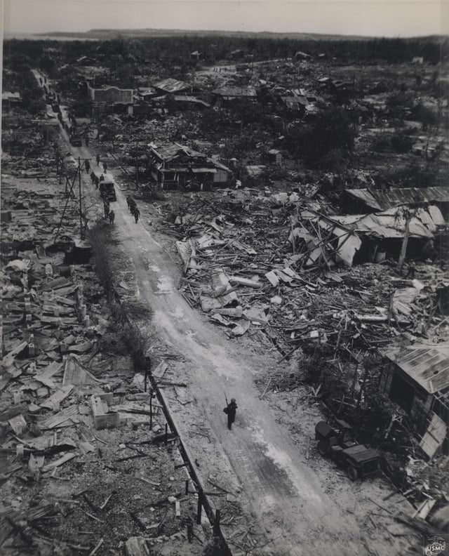 A column of U.S. Marines passes through the remains of a small town on Tinian. 31 July 1944 [2322 × 2875]