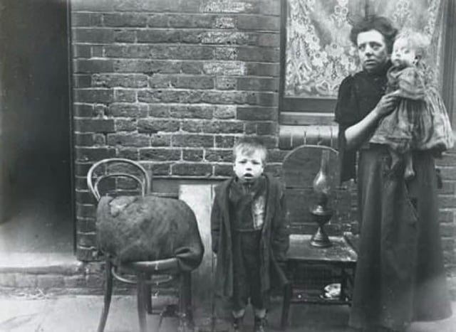 Evicted, exhausted, with nowhere left to turn, this East End matchbox maker stands beside her few possessions and two young children, c.1900, unknown photographer. Women like her worked punishing hours for desperately low pay, often making boxes at home by candlelight while caring for their families